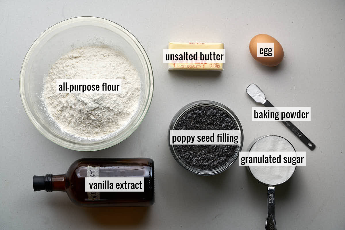 Poppy seeds, flour, an egg, a wrapped stick of butter, and other ingredients on a countertop to make cookies.