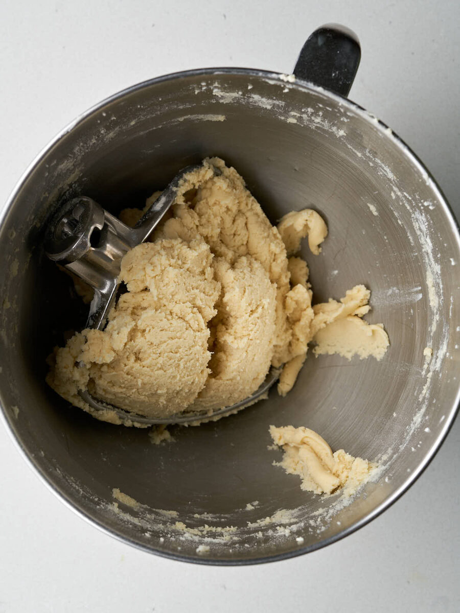 Cookie dough in a metal stand mixer bowl with the metal paddle inside.