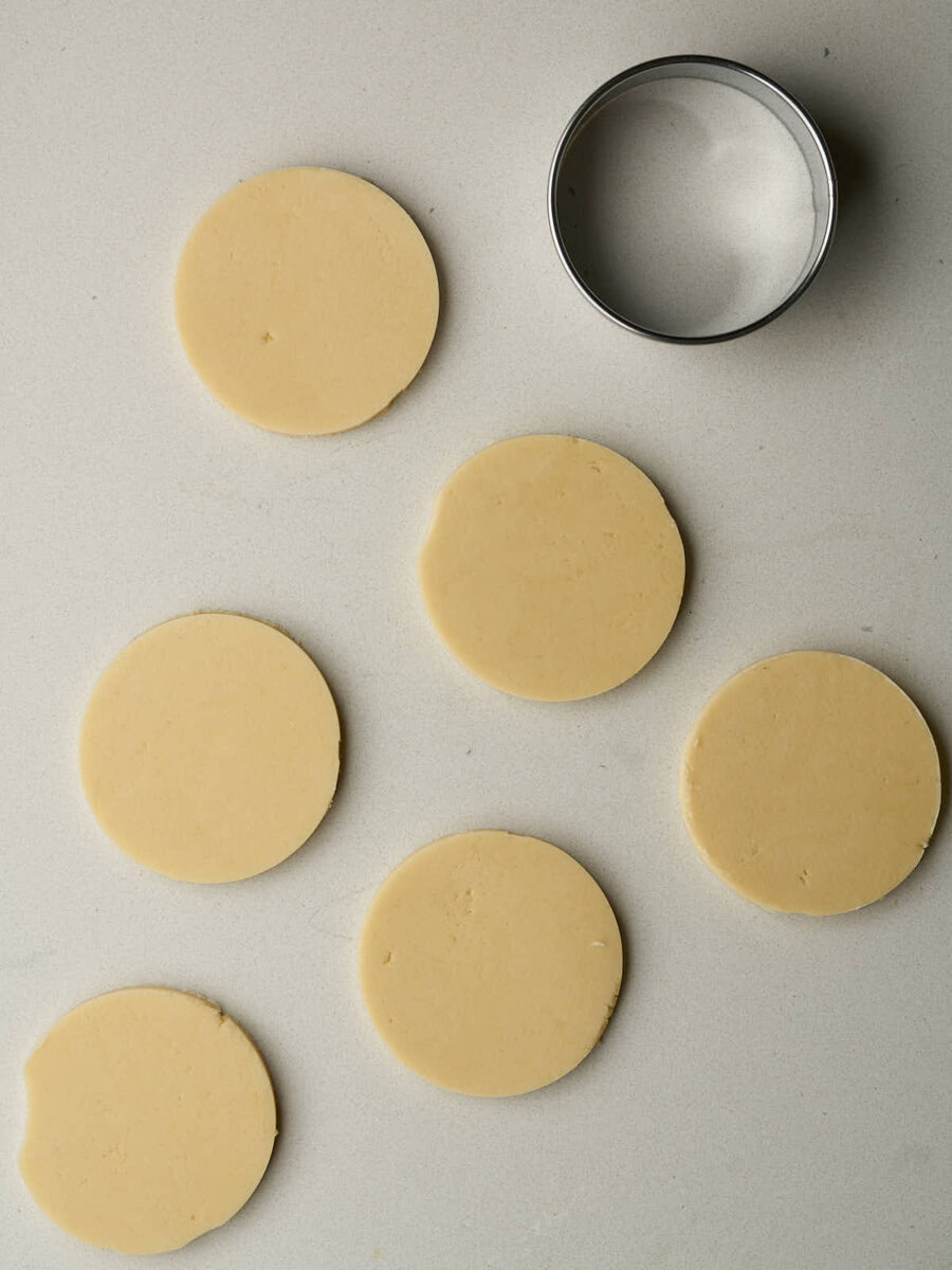 Circles of dough next to a round cookie cutter.