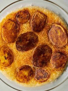 Glass plate of yellow crispy rice dotted with crispy, cooked slices of potato.