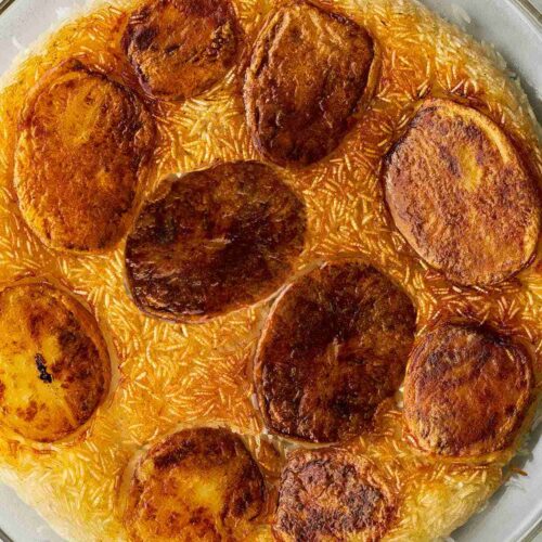 Glass plate of yellow crispy rice dotted with crispy, cooked slices of potato.