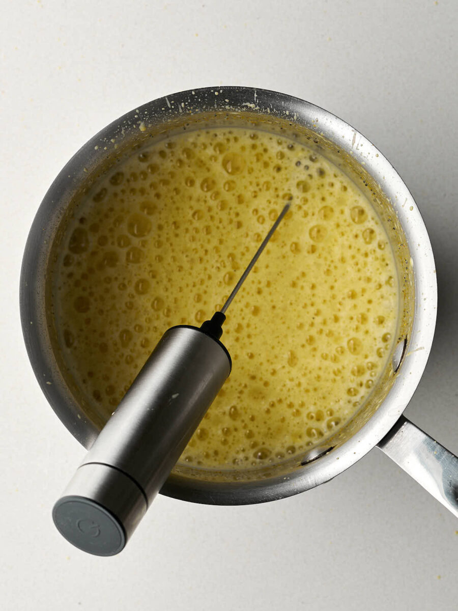 Frothed yellow liquid in a saucepan with a handheld frother.