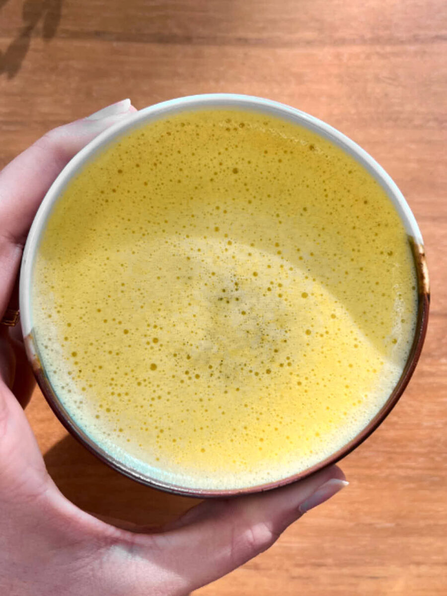 A yellow latte in a hand over a wood background.